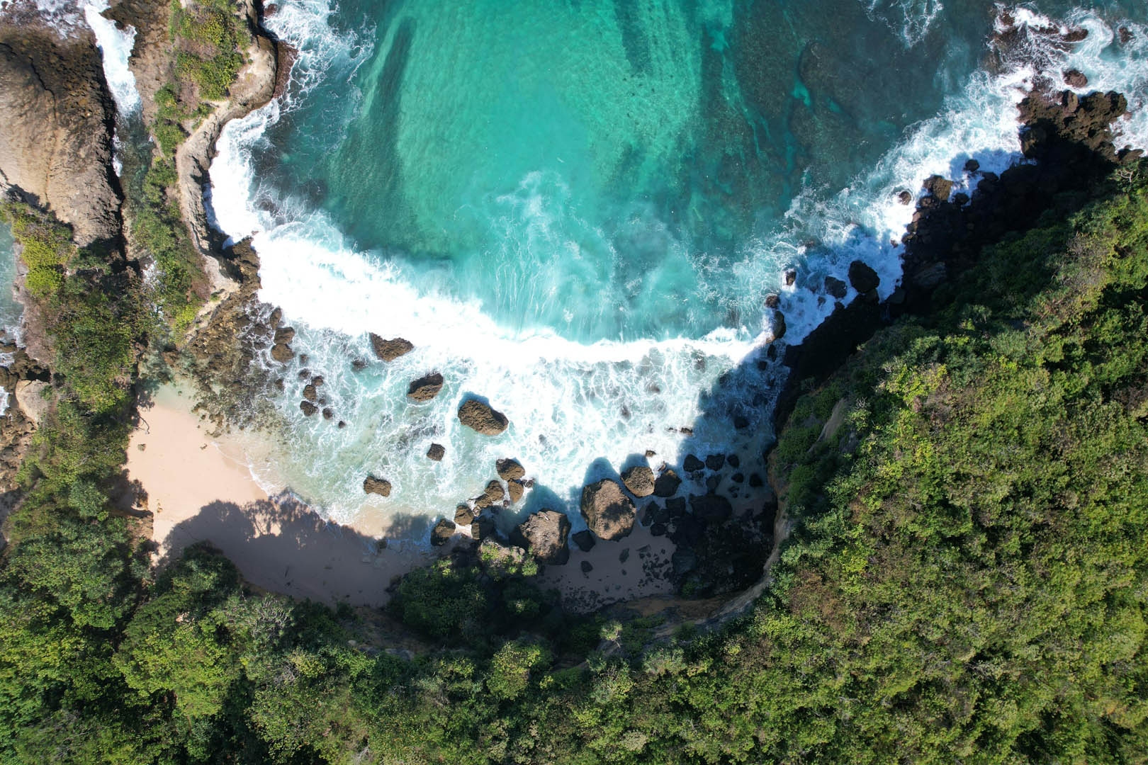 Aerial view of Kabisu’s hidden beach and turquoise waters surrounded by lush cliffs in Southwest Sumba