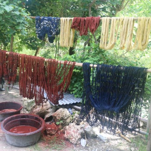 Naturally dyed yarns in indigo, morinda red, and yellow drying outdoors in Sumba.