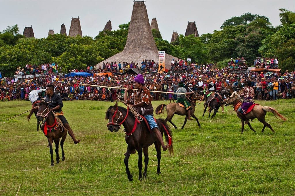 Pasola Festival in Sumba with horsemen, traditional houses, and large crowd of spectators