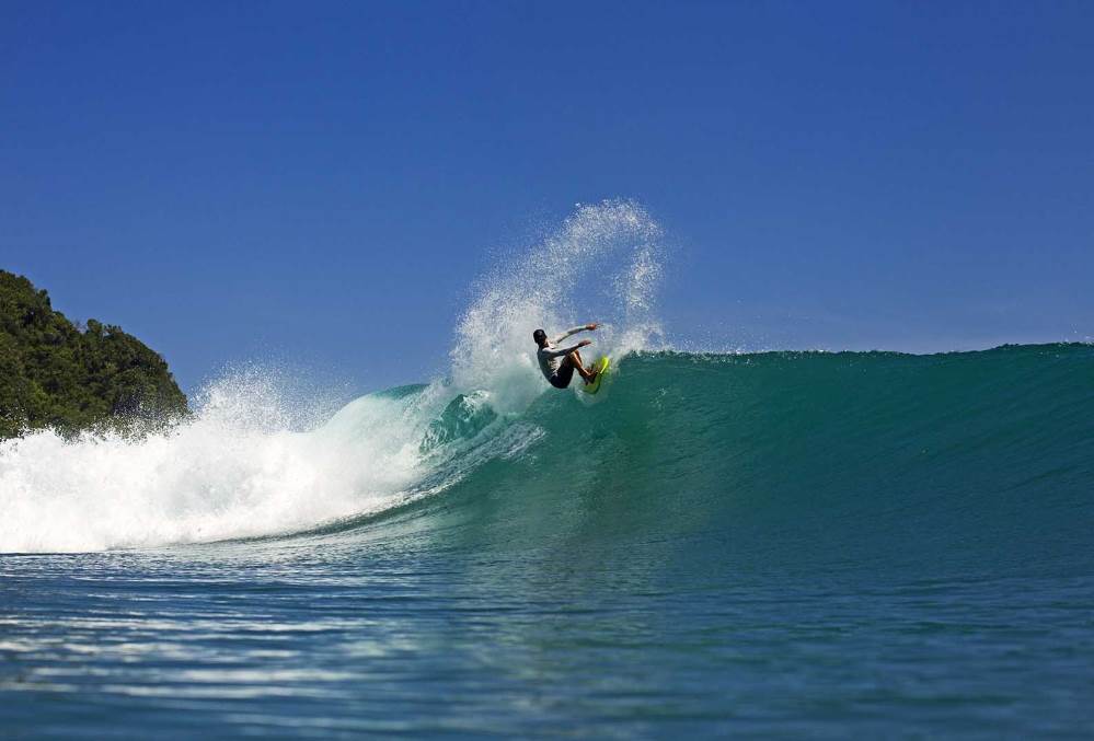Surfer riding perfect turquoise wave at Occy’s Left surf break in Sumba, Indonesia