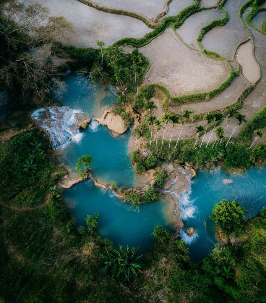 Aerial view of blue lagoon and cascading waterfall surrounded by rice paddies in Sumba