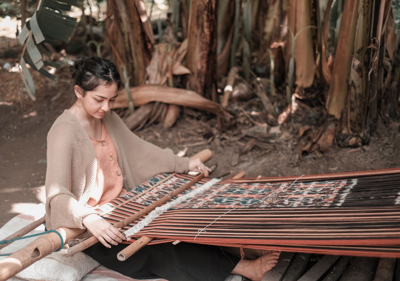 A young woman weaving ikat fabric on a backstrap loom in Sumba.