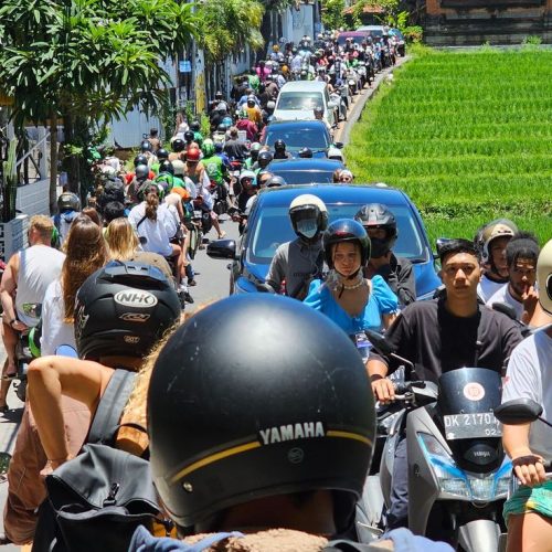 Crowded street in Canggu, Bali, with motorbikes and cars stuck in heavy traffic next to rice fields.