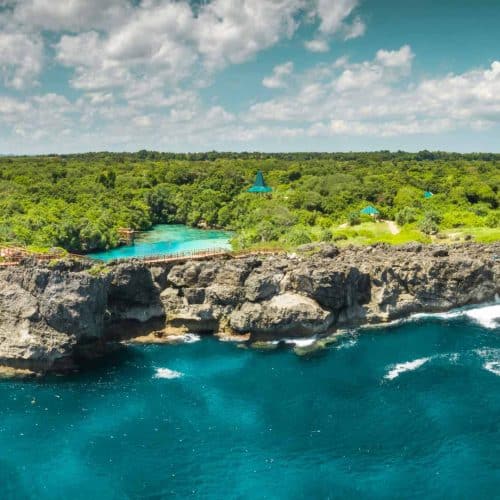 Aerial view of rugged cliffs and a bright turquoise lagoon surrounded by dense green forest on Sumba, Indonesia.
