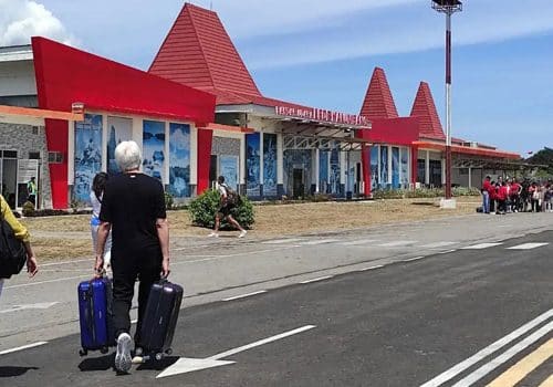 Passengers walking with luggage in front of Tambolaka Airport terminal on Sumba island.